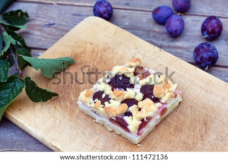 Fresh baked sweet plum cake on cutting board and fresh plums on wooden old table