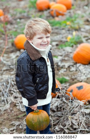 Happy little toddler boy on pumpkin field on cold autumn day with green pumpkin in hand