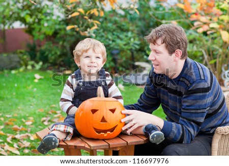 Young man and toddler boy making jack-o-lantern for halloween in autumn garden