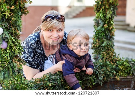 Beautiful young woman and little son in spring near fountain decorated with Easter eggs