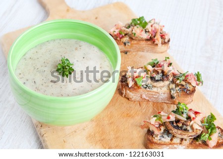 Fresh cream cauliflower soup in green bowl with fresh baked bread with apples, mushrooms, cheese and parsley on wooden board