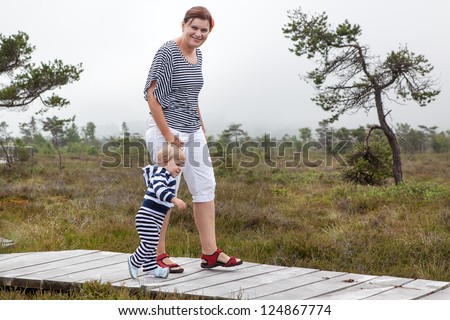 Little baby boy making his first steps with mother in nature park