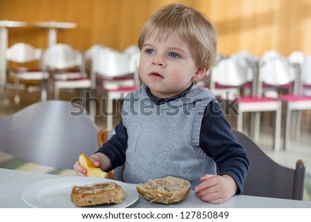 Little boy with eating bread and apple in kindergarten for breakfast