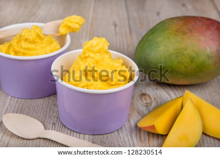 Serving of frozen homemade creamy ice yoghurt  with fresh mango and wooden spoon
