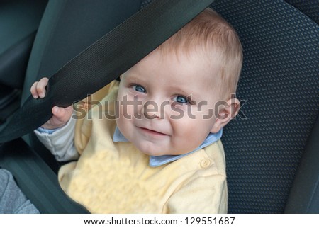 Adorable baby boy with blue eyes sitting in car, summer.