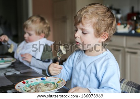 Two little brother boys eating pasta meal in home kitchen. Selective focus