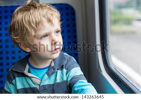 Beautiful toddler boy looking out train window outside, while it moving. travel