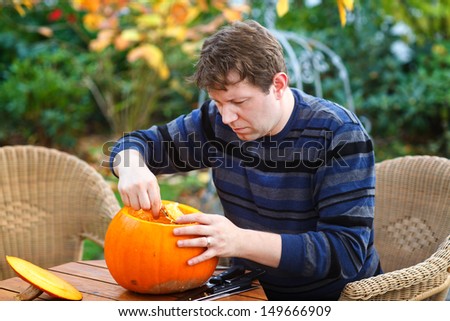 Young man making jack-o-lantern pumpkin for halloween in autumn garden