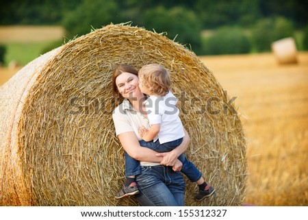 Young mother and her little son having fun on yellow hay field in summer