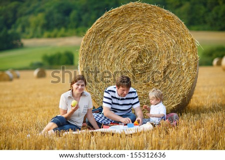 happy family of three picnicking on yellow hay field in summer