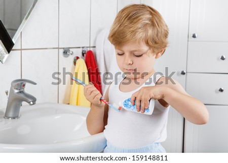 Cute toddler boy with blue eyes and blond hair brushing his teeth at home