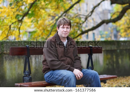 Portrait of beautiful young man in the autumn park sitting on bench