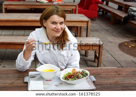 Young woman eating soup and salad in outdoor restaurant