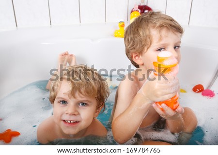 Two adorable little twin boys having fun with water by taking bath in bathtub