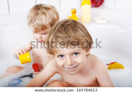 Two little twin boys having fun with water by taking bath in bathtub
