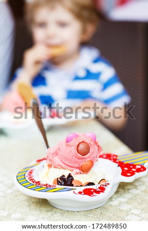 Pink ice-cream for children with colorful chocolate drops with kid on background. Selective focus on ice.