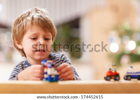 Little blond boy playing with cars and toys at home, indoor