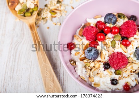 Fresh yoghurt with home made cereals and muesli, fresh raspberry and blueberry on wooden textured background as healthy breakfast