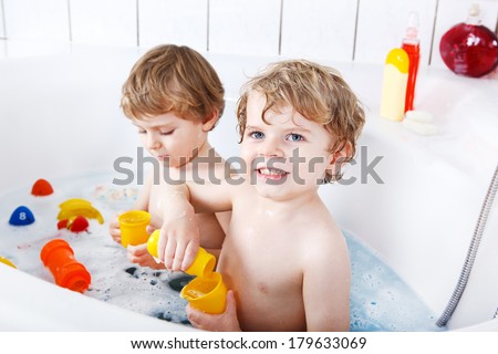 Two adorable little twin boys having fun with water by taking bath in bathtub