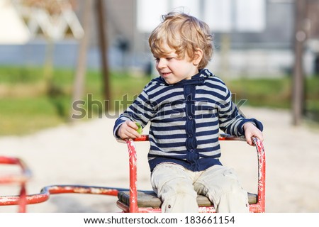 Little toddler boy having fun on old carousel on outdoor playground.