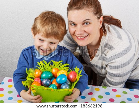 Little toddler boy and his mother having fun with preparing eggs for Easter egg hunt, traditional action in Germany for Eastern holiday, indoors