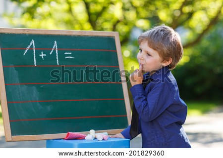 Serious little boy at blackboard practicing mathematics, outdoors. Back to school concept.