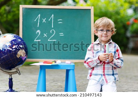 Little boy at blackboard practicing mathematics, outdoor school or nursery. Back to school concept