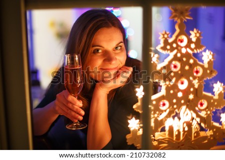 Portrait of young woman through window celebrating New Year\'s Eve and drinking champagne