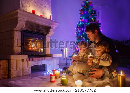 Young father and his two little children sitting by a fireplace at home on Christmas time