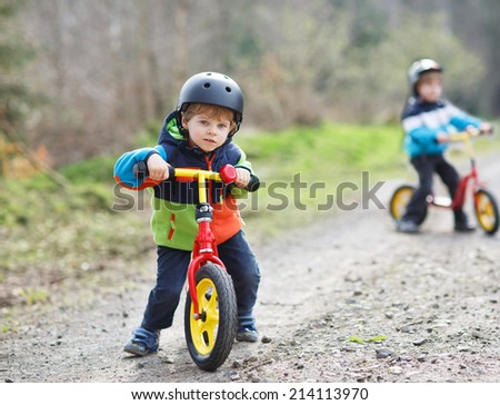 Two active little sibling boys having fun on bikes in forest on cold day.