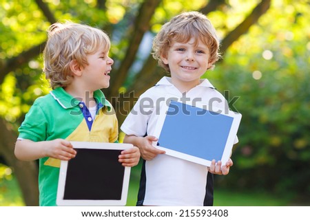 Two happy little sibling kids holding tablet pc, outdoors. Brother boys playing together.