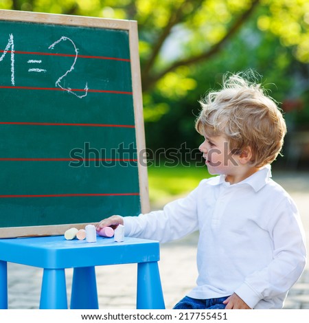 Adorable little toddler child at blackboard practicing mathematics, outdoor school or nursery. Square format.