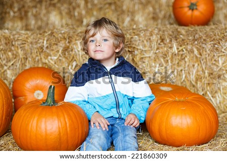 Little cute kid boy sitting with huge pumpkin on halloween or thanksgiving harvest festival or patch, outdoors