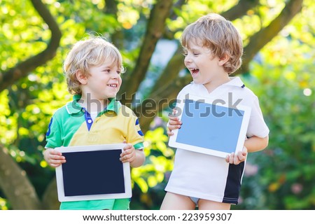 Two happy little boy friends holding tablet pc, outdoors. Kids playing together.