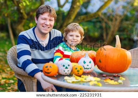 Young dad and his little son making jack-o-lantern for halloween in autumn garden, outdoors. Family having fun together