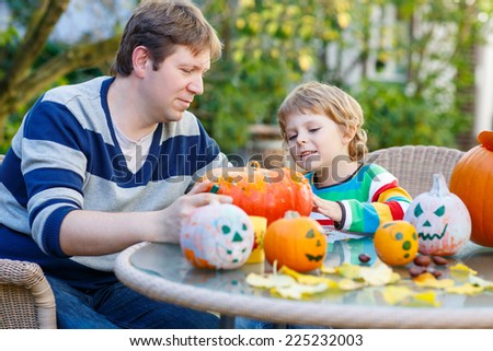 Cute kid boy and his father making jack-o-lantern for halloween in autumn garden, outdoors. Family having fun together