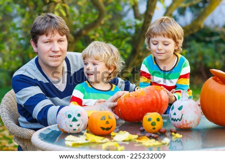 Young father and his two kid boys making jack-o-lantern for halloween in autumn garden, outdoors. Happy family of three having fun together