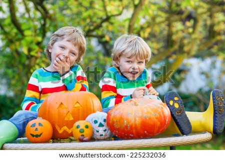 Two little twin boys making jack-o-lantern for halloween in autumn garden, outdoors. Happy family having fun together