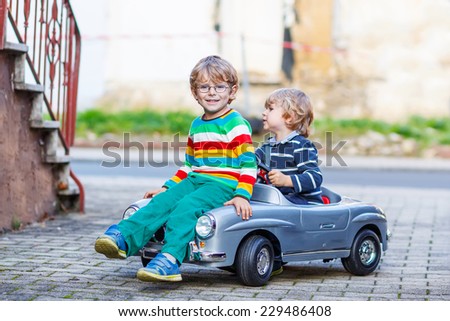 Two happy kid boys playing with big old toy car in summer garden, outdoors. Siblings and friends on warm day.