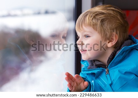 Beautiful toddler boy looking out train window outside, while it moving. Going on vacations and traveling by railway in winter.