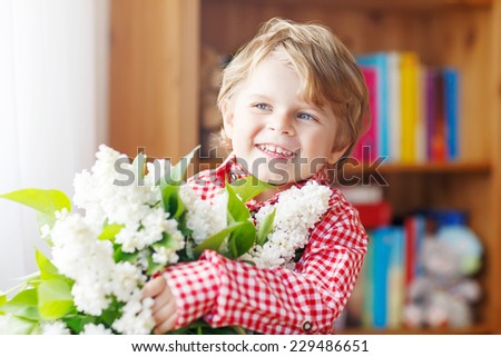 Adorable smiling little toddler boy with blooming white lilac flowers, indoor. Mother\'s day, father\'s day or valentine\'s day concept.