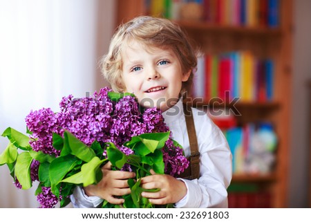 Adorable smiling little boy with blooming purple lilac flowers, indoor. Mother\'s day, father\'s day or valentine\'s day concept.