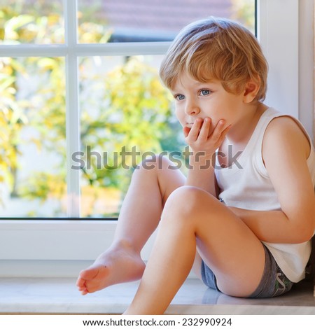 Little boy of three years looking out of the window on yellow autumn tree. Square format.
