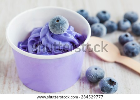 Serving of frozen creamy ice yoghurt  with whole fresh blueberries and wooden spoon with selective focus. Healthy sweet dessert with organic berries.