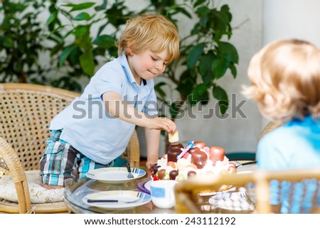 Little adorable boy celebrating with brother his third birthday in home\'s garden with big cake. Happy child laughing about gifts and tasting cake. Outdoors on sunny day.