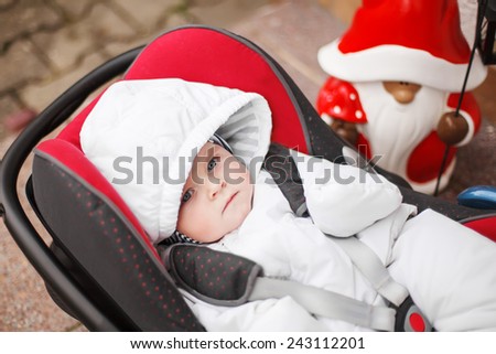 Little baby toddler in white winter clothes sitting in car seat. On cold winter day. Children safety in car concept.