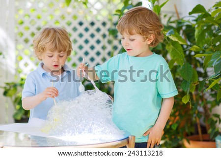 Two adorable friend boys making experiment with colorful soap bubbles and water, outdoors. On warm sunny day children playing together. Creative leisure with kids in summer, outdoors.Child development