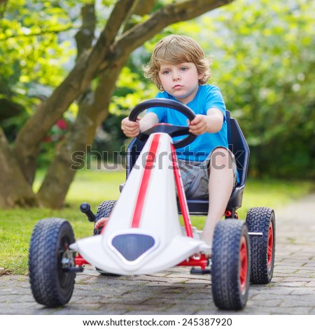 Funny little boy having fun and driving toy race car in home\'s garden. Active games for children in summer. On warm sunny day.