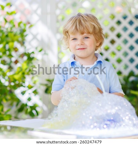 Happy little boy making experiment with colorful soap bubbles and water, outdoors.