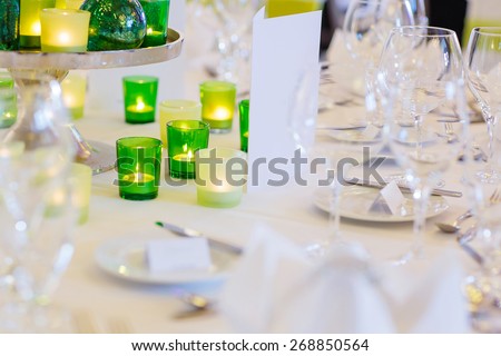 Elegant table set in green and white for wedding or event party. Flower arrangements, candles, china and porcelain tableware and napkins. Wedding details.